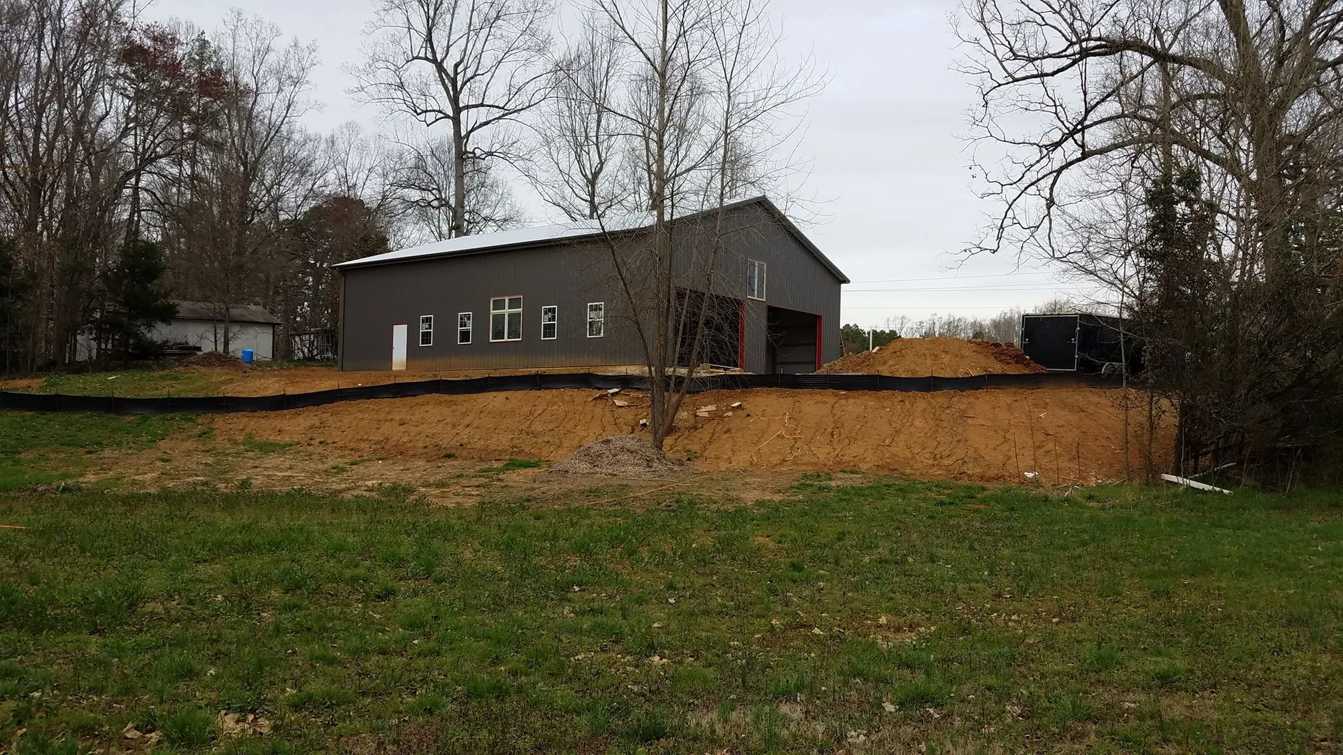 A new gray building with multiple windows sits on a freshly excavated lot with bare earth in the foreground.