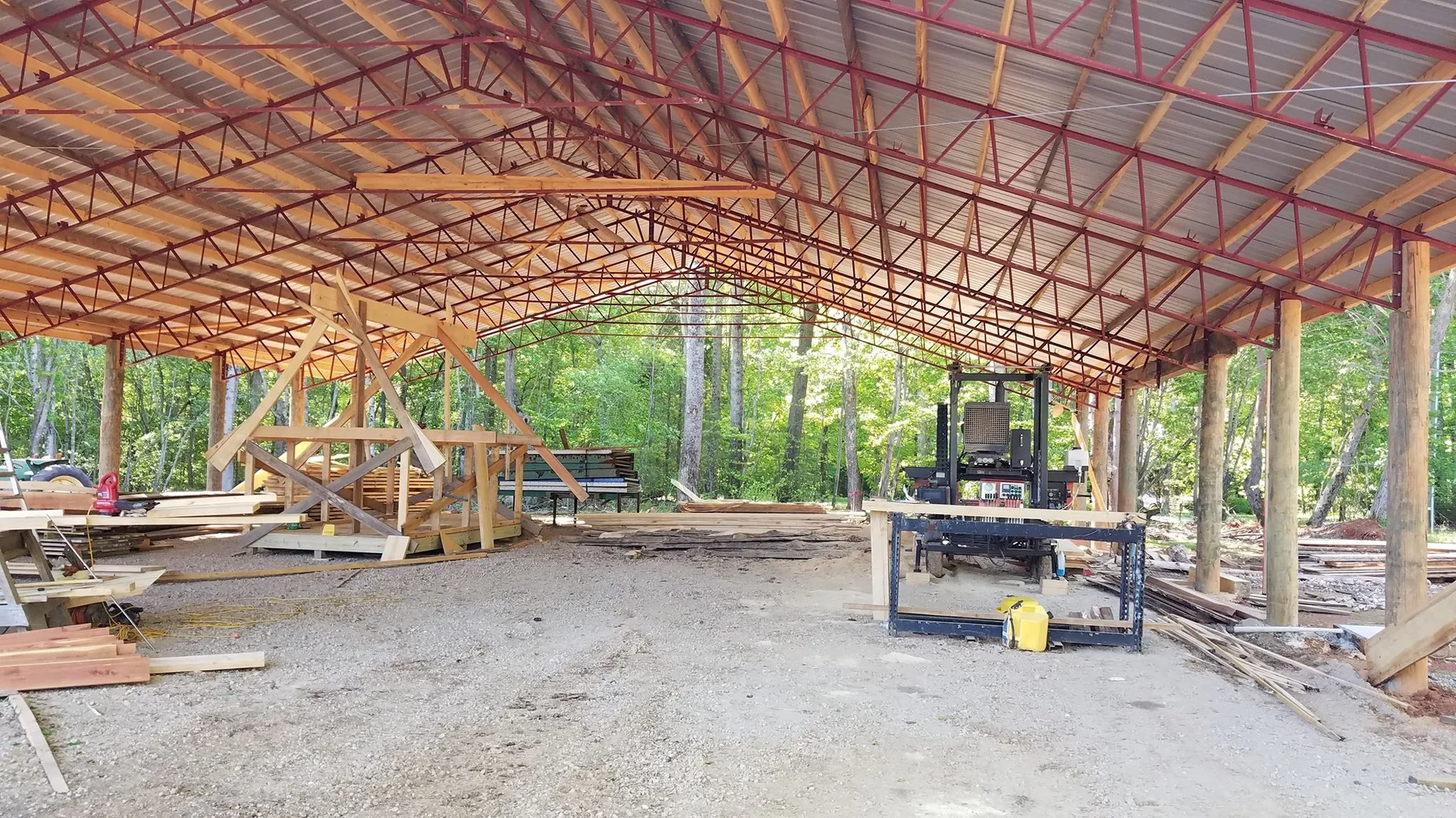 The image shows a large open metal-framed structure under construction with wooden beams and construction materials scattered around the site.