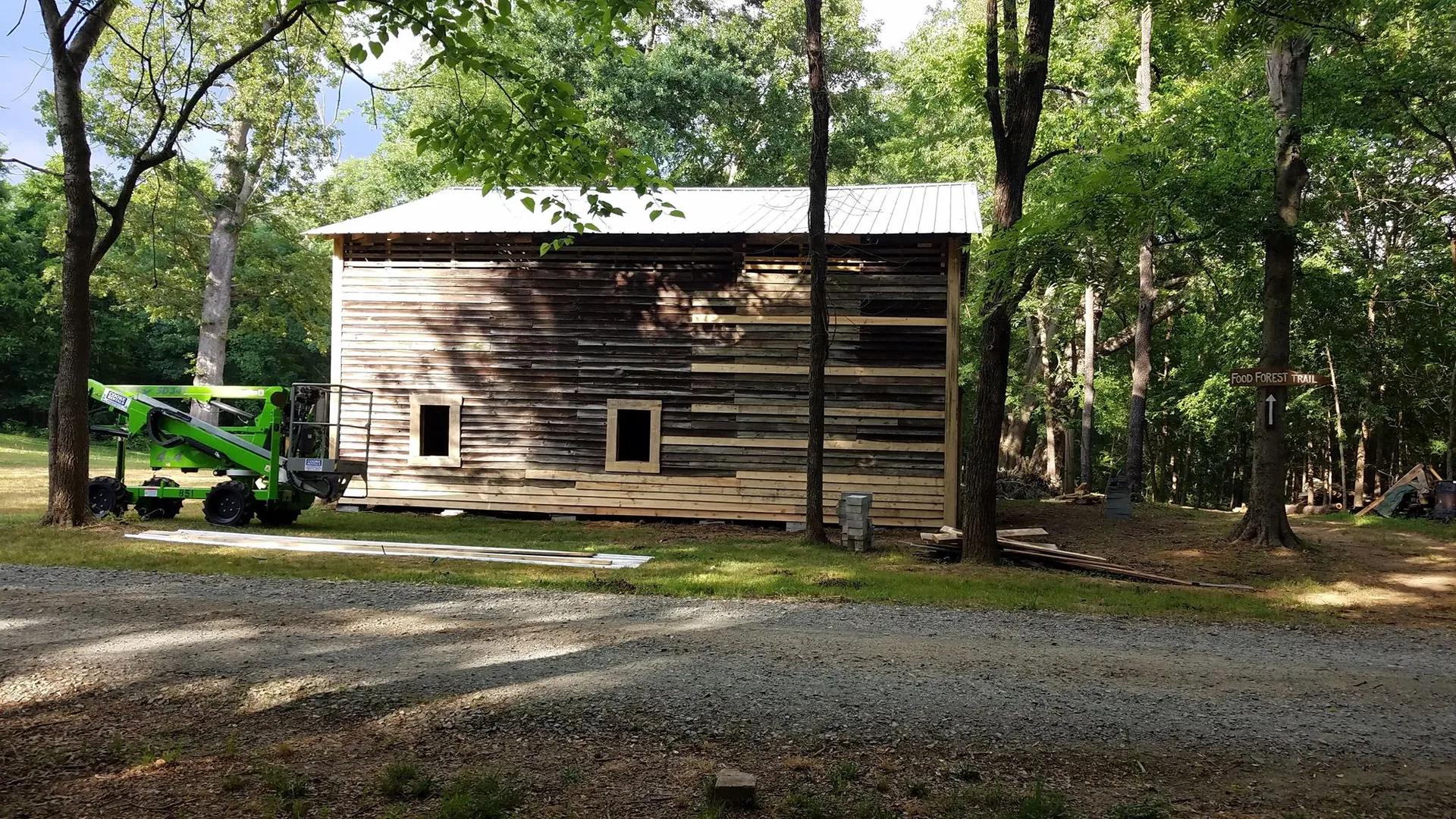 A wooden cabin undergoing renovations in a forested area with construction equipment nearby.