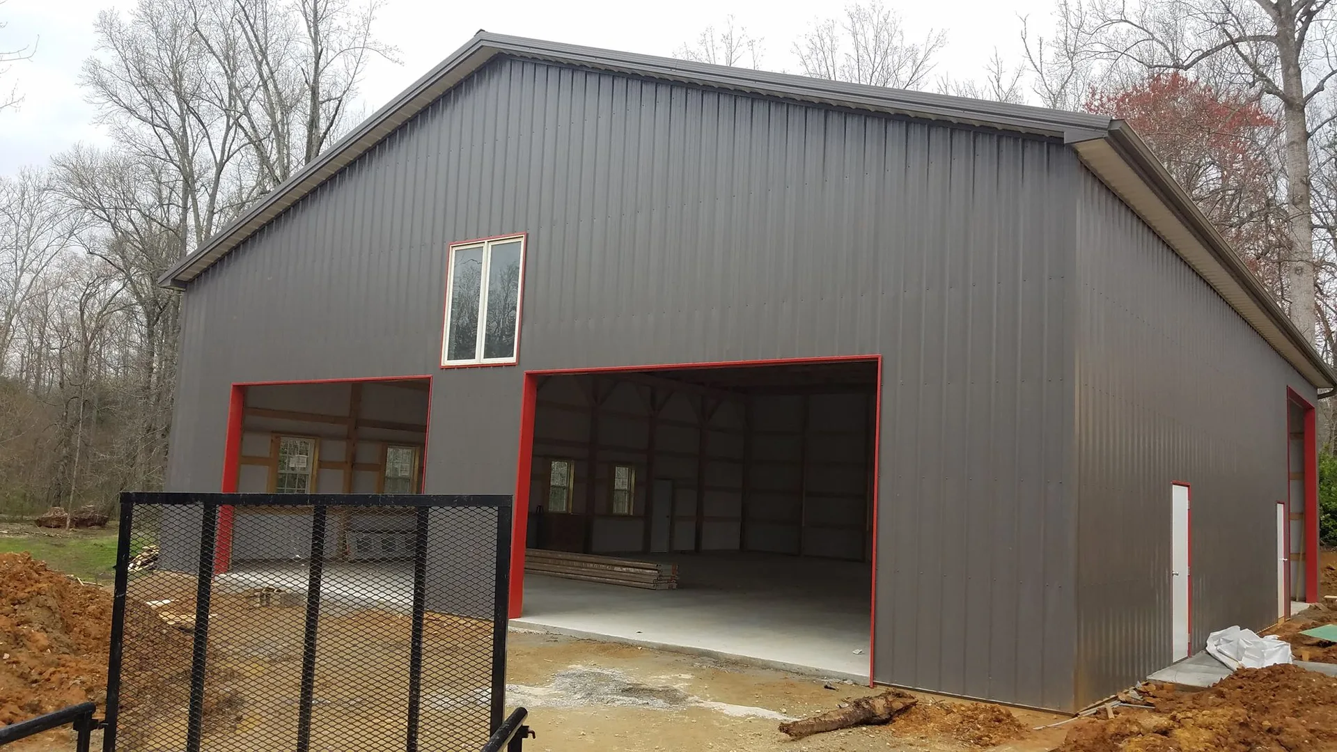 A large metal building with red trim and an open garage door, surrounded by a natural landscape with a cloudy sky.