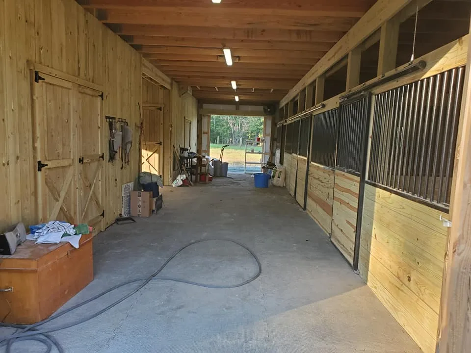 A tidy horse stable interior with equipment storage on the left and stall doors on the right.