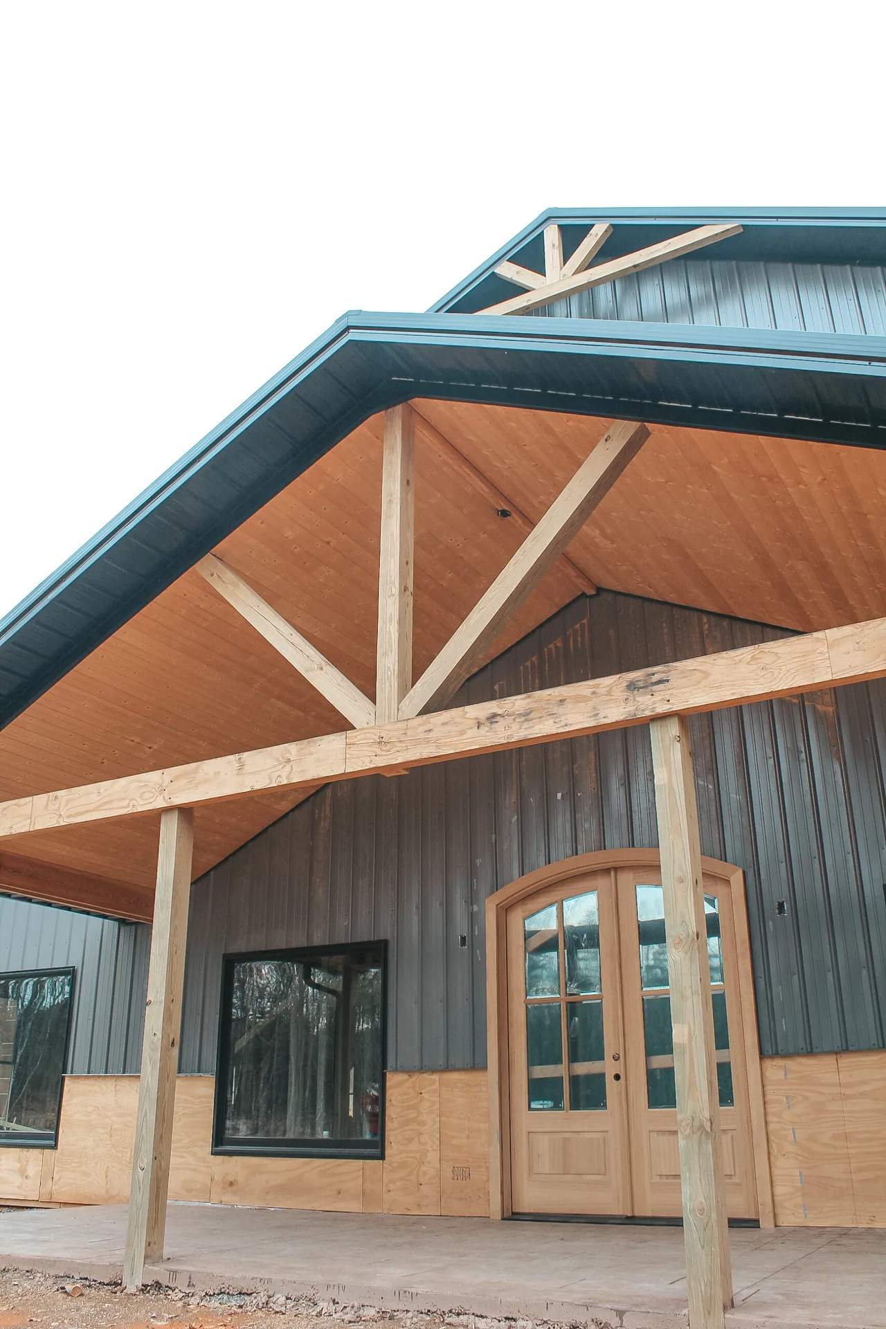 The image shows the exterior of a modern building with a wooden facade and a large entrance door under a covered porch.