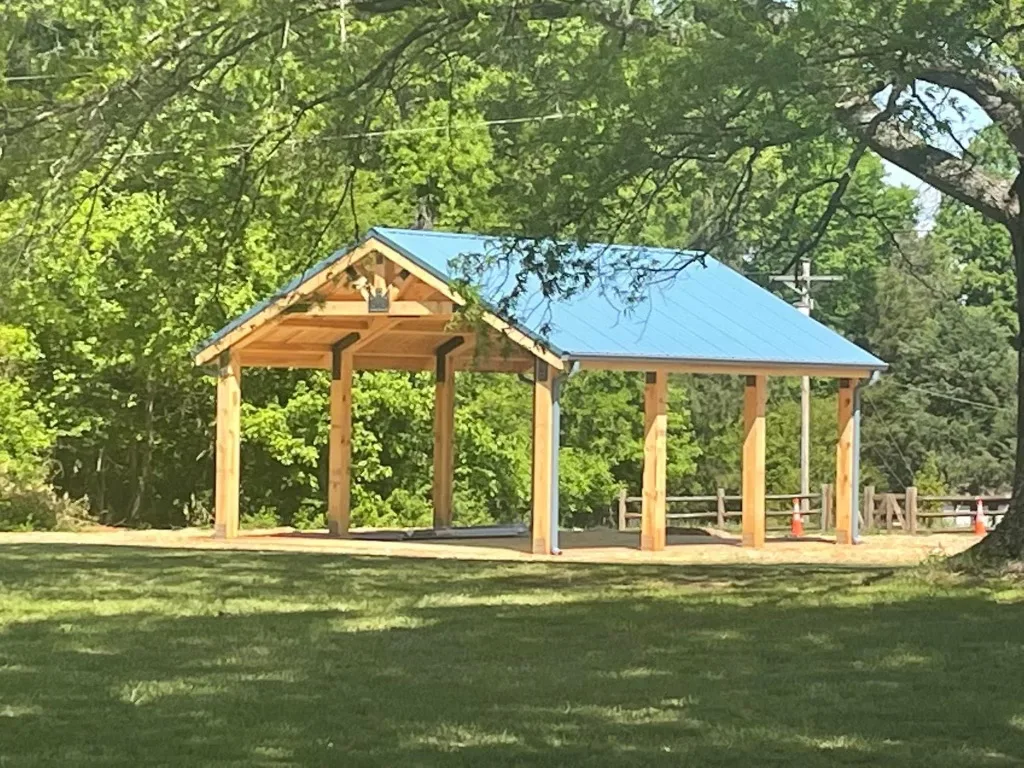 A newly constructed wooden pavilion with a blue roof, located in a lush green park setting.