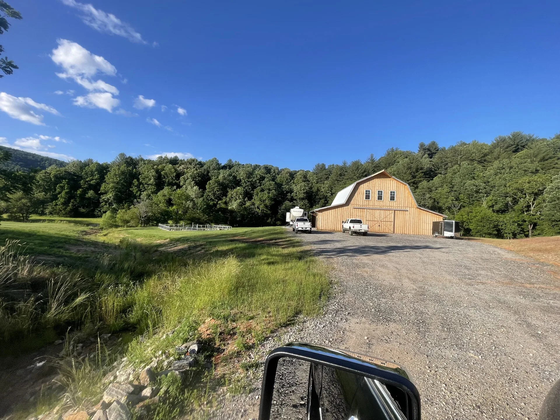 A large barn with a white truck parked beside it, surrounded by greenery under a clear blue sky.