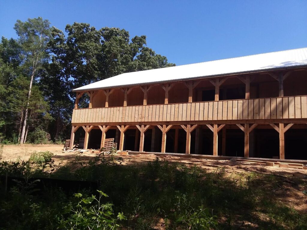 A large two-story wooden building with a covered balcony, surrounded by trees under a clear blue sky.